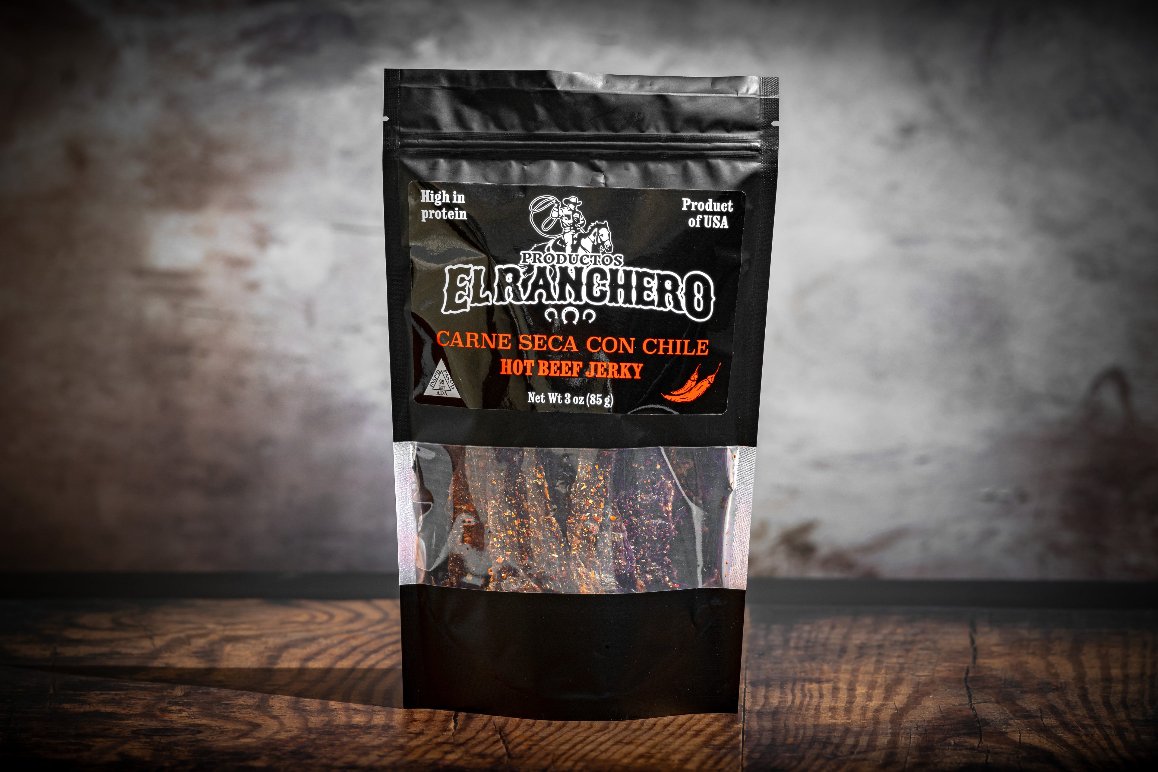 El Ranchero Carne Seca Con Chile hot beef jerky package on a wooden surface with a blurred background